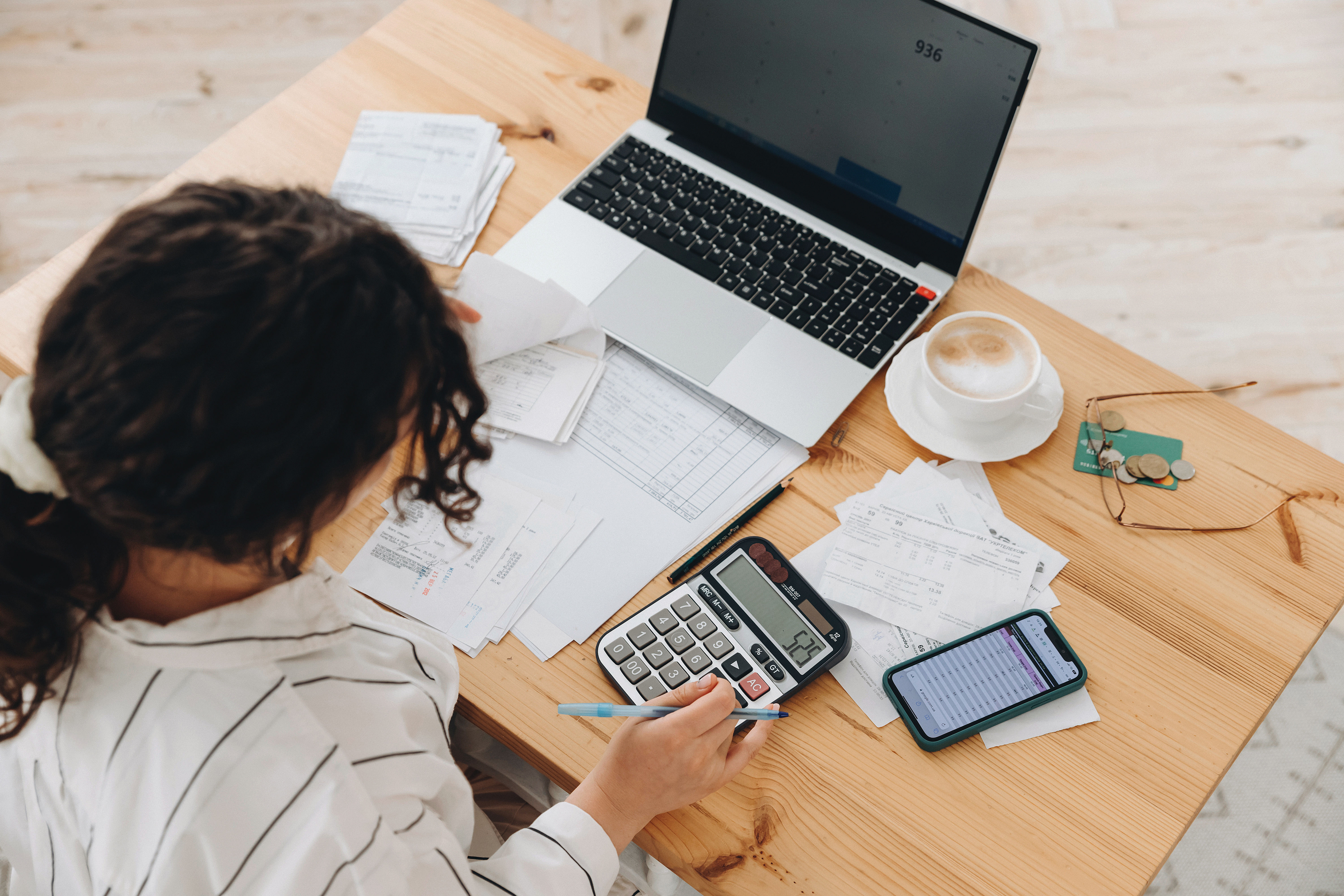 how to create a personal budget; woman at desk budgeting with computer, calculator, papers in view- arial view