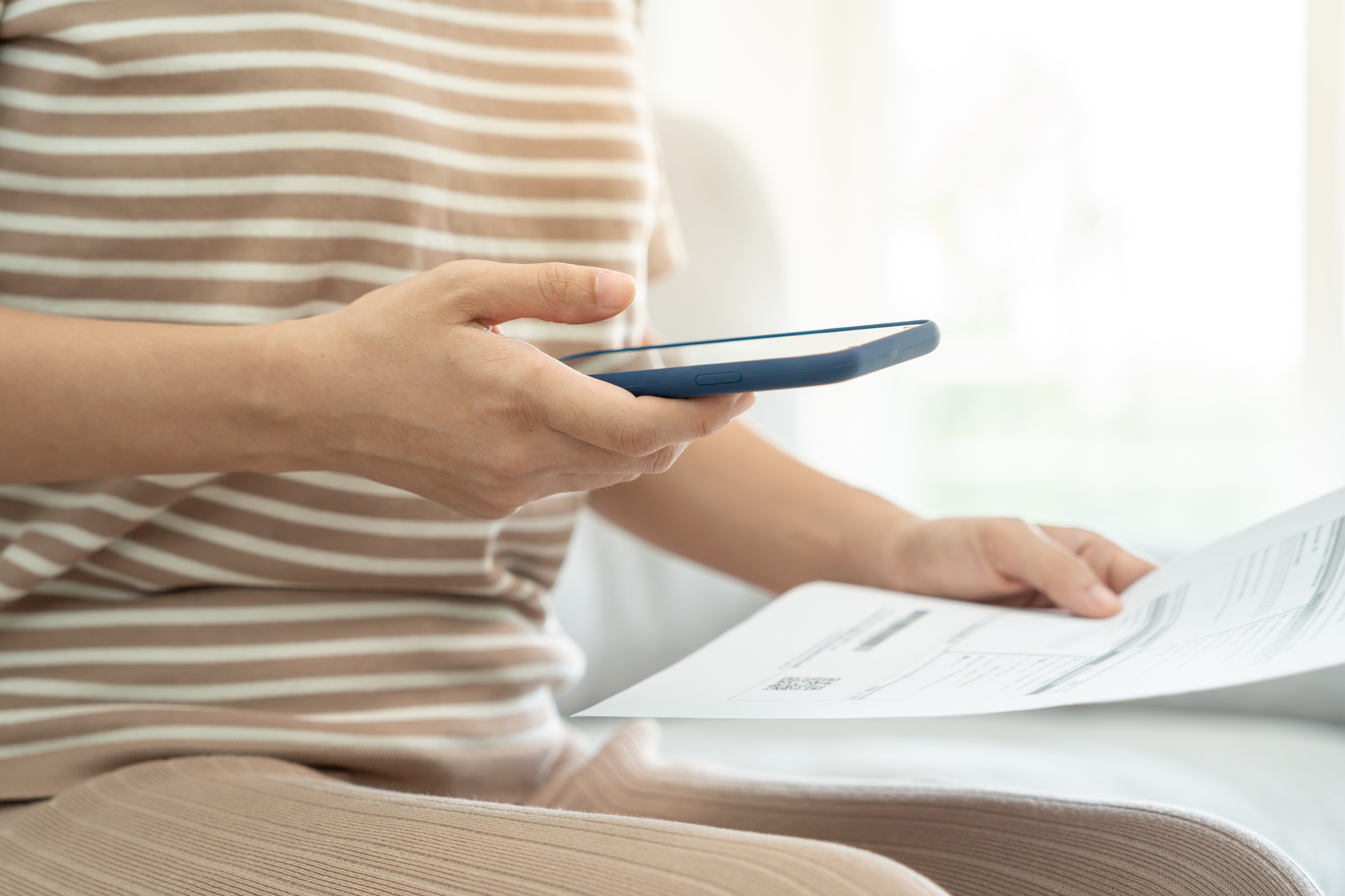 woman's hand on phone paying bills with qr code online; transferring her online bills to a new bank account